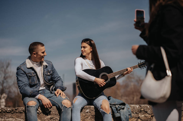 Крупним планом дівчина фотографує музичну пару, що сидить на річці в місті - Фото, зображення