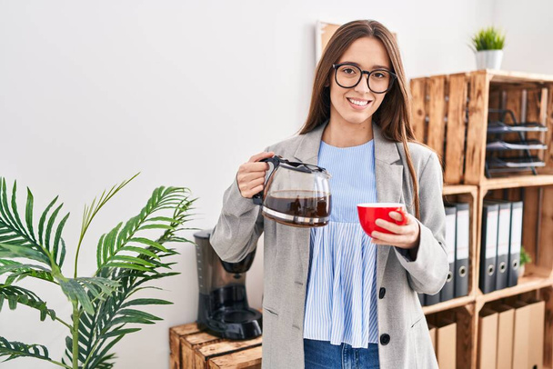Молодая красивая латиноамериканка-предприниматель наливает кофе на чашку кофе в офисе - Фото, изображение