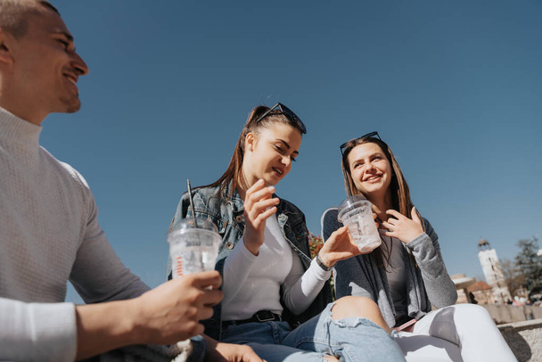 Close up of group of three friends smiling and sitting at the center of the city and drinking milkshakes - Fotografie, Obrázek