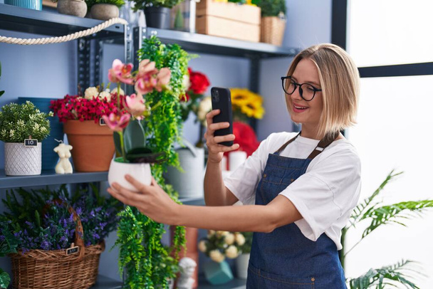 Молодая блондинка флорист сделать фото на смартфоне, чтобы посадить в цветочный магазин - Фото, изображение