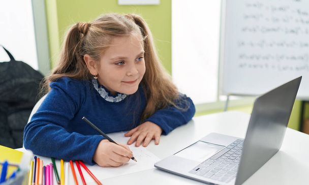 Sınıfta dizüstü bilgisayar kullanan sevimli sarışın kız öğrenci. - Fotoğraf, Görsel