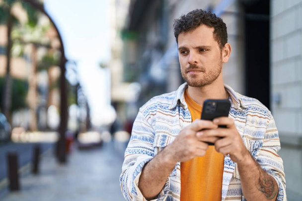 ストリートでスマートフォンを使う若いヒスパニック系の男 - 写真・画像