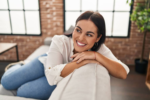 Νέα όμορφη ισπανόφωνη γυναίκα χαμογελά αυτοπεποίθηση κάθεται στον καναπέ στο σπίτι - Φωτογραφία, εικόνα