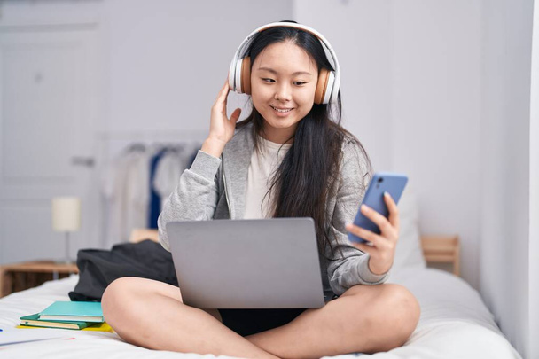 Giovane donna cinese che ascolta musica utilizzando smartphone in camera da letto - Foto, immagini