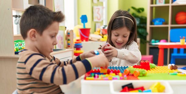 Uroczy chłopiec i dziewczyna bawią się klockami budowlanymi siedzącymi na stole w przedszkolu - Zdjęcie, obraz
