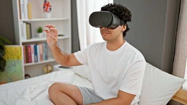 Молодий латинський чоловік грає у відеоігри, використовуючи окуляри віртуальної реальності в спальні - Фото, зображення