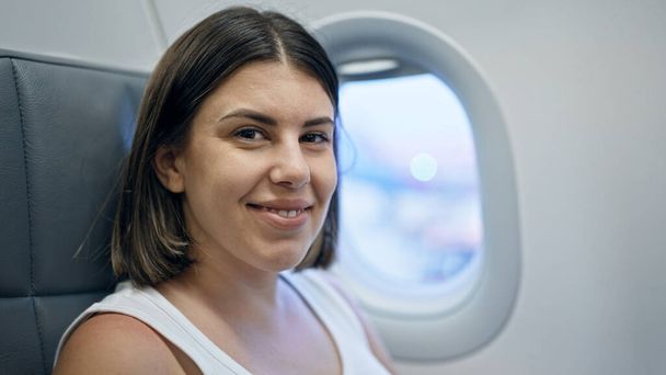 Joven hermosa mujer hispana sonriendo sentada en el avión - Foto, Imagen