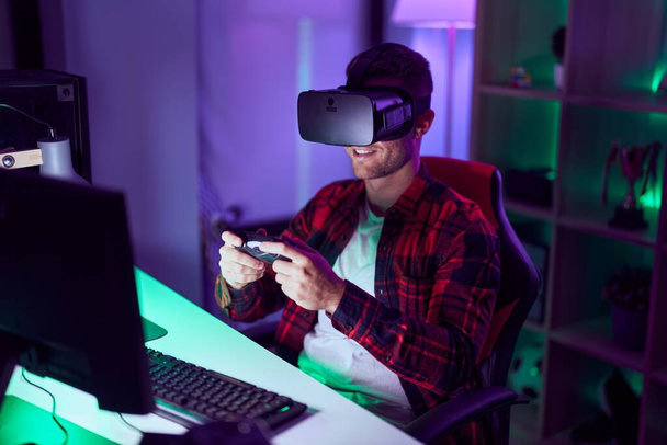 Νεαρός καυκάσιος άνθρωπος streamer παίζει βιντεοπαιχνίδι χρησιμοποιώντας γυαλιά εικονικής πραγματικότητας και joystick στο gaming room - Φωτογραφία, εικόνα