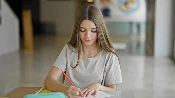 Νεαρό όμορφο κορίτσι φοιτητής που γράφει στο σημειωματάριο σκέψης στη βιβλιοθήκη - Φωτογραφία, εικόνα