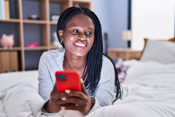 African american woman using smartphone lying on bed at bedroom - Foto, immagini