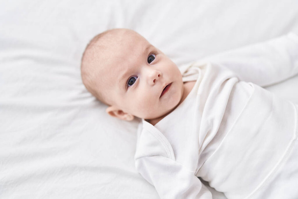 Adorável bebê caucasiano deitado na cama com expressão relaxada no quarto - Foto, Imagem