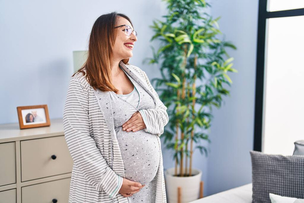 Giovane donna incinta sorridente fiducioso commovente pancia a casa - Foto, immagini