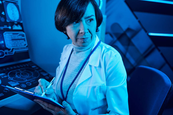 Futuristic Expertise: Senior Woman Scientist Records Data and Contemplates in Future Science Center - Photo, Image