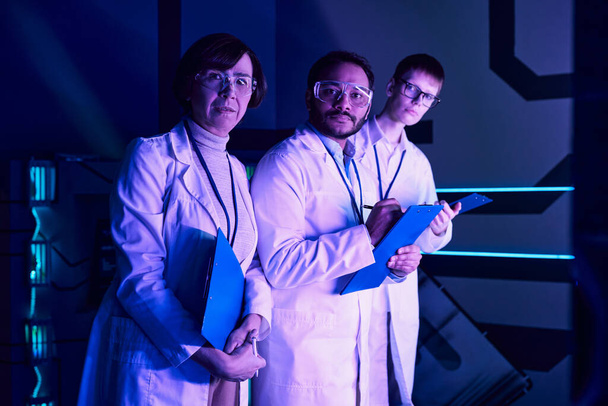 Futuristische Focus: Drie Wetenschappers betrekken in Headshot Analyse binnen Neon-Lit Science Center. - Foto, afbeelding