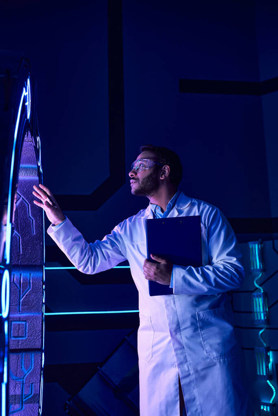 Zukunftswissenschaft: Indischer Wissenschaftler mit Brille untersucht neue Geräte in neonbeleuchtetem Innovationszentrum - Foto, Bild