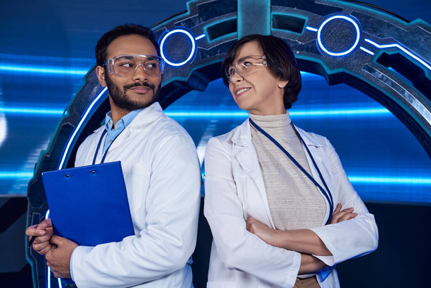 καινοτόμο εργαστήριο, πολυεθνικοί επιστήμονες χαμογελώντας ο ένας στον άλλο κοντά σε πειραματική συσκευή με νέον φως - Φωτογραφία, εικόνα