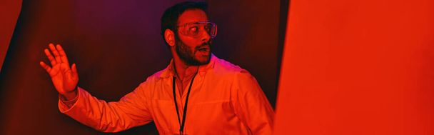 испуганный индийский ученый смотрит в сторону в красный неоновый свет, неизвестный феномен, баннер - Фото, изображение