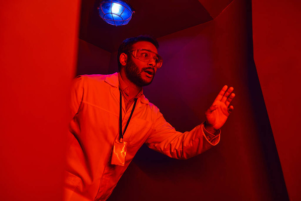 geschokte Indiase wetenschapper in rood neon licht in rood neon licht, onbekend fenomeen - Foto, afbeelding