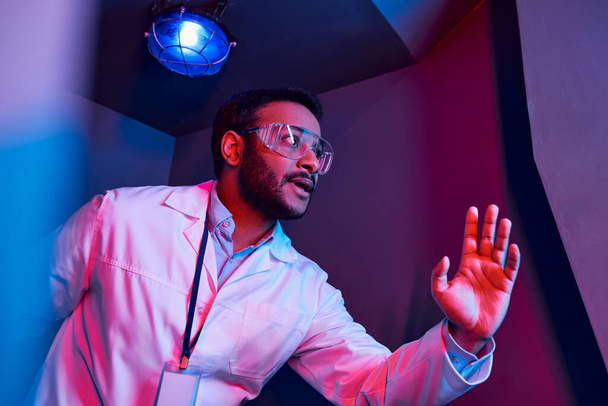 esplorazione futura, preoccupato scienziato indiano guardando lontano nella luce al neon in hub di innovazione - Foto, immagini