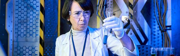 középkorú nő tudós szemüvegben nézi folyadék kémcsőben innovációs labor, banner - Fotó, kép