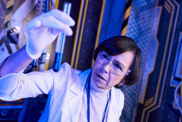 badając życie pozaziemskie, kobieta naukowiec trzyma probówkę z próbką cieczy w futurystycznym laboratorium - Zdjęcie, obraz