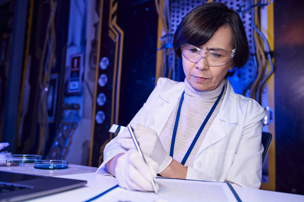 toekomstige wetenschap, vrouw wetenschapper schrijven op klembord in de buurt van buitenaardse monsters in petrischaaltjes - Foto, afbeelding