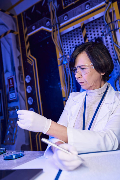 mujer científica en gafas mirando el papel de tornasol, explorando la vida extraterrestre en laboratorio innovador - Foto, Imagen