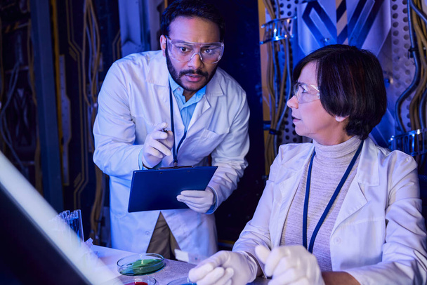 indyjski naukowiec wskazujący na próbki na szkle laboratoryjnym w pobliżu kolegi badającego życie pozaziemskie - Zdjęcie, obraz