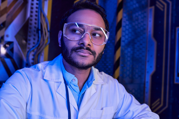 futuristisches Konzept, Porträt eines bärtigen indischen Wissenschaftlers mit Brille, der im Science Center wegschaut - Foto, Bild