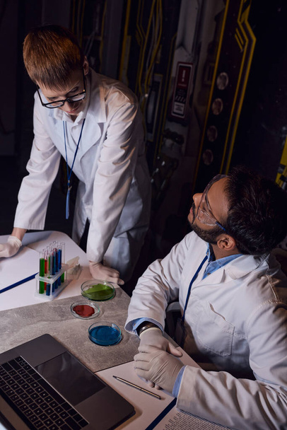 científicos multiétnicos que trabajan cerca de tubos de ensayo, placas de Petri y portátil en laboratorio innovador - Foto, Imagen