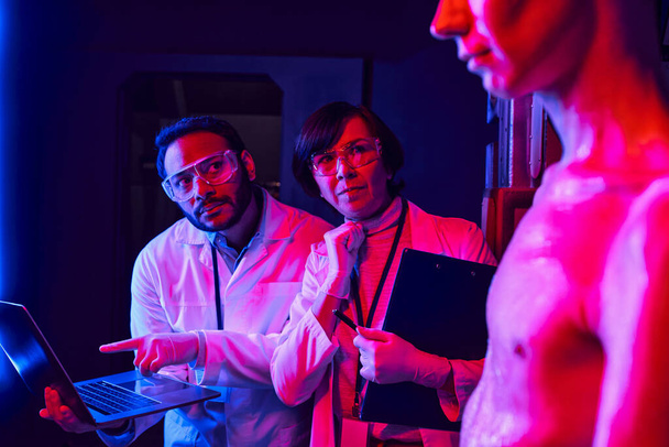 indischer Wissenschaftler zeigt auf Laptop neben nachdenklichem Kollegen und Alien im Entdeckungszentrum - Foto, Bild