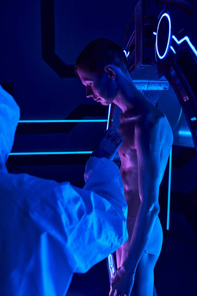 kosmisch fenomeen, wetenschapper in hazmat pak raakt humanoïde alien in neon-verlicht innovatie hub - Foto, afbeelding