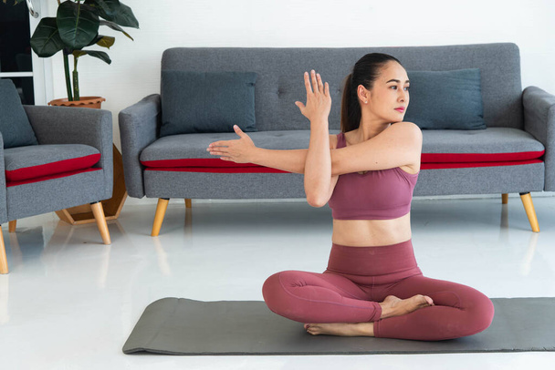 Asiatische junge gesunde Frau in Sportbekleidung praktiziert Yoga zu Hause, Sportmädchen meditiert im Wohnzimmer zu Hause - Foto, Bild