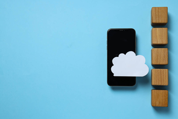 smartphone nero con carta nuvola bianca e tazze di legno su sfondo blu, posto per il testo - Foto, immagini