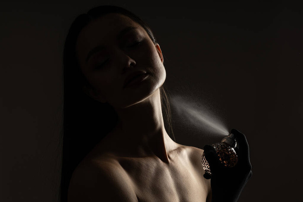 Young woman applying perfume on black background - 写真・画像