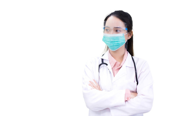 白い実験室のコートの若い専門のアジアの女性の医者は白い背景で隔離された働いている間コロナウイルスCovidおよびヘルスケアを保護するために医学の表面のマスクおよび表面盾を身に着けます. - 写真・画像