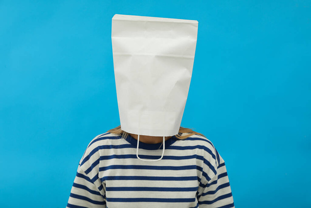 Girl with paper bag on head on blue background - Foto, afbeelding
