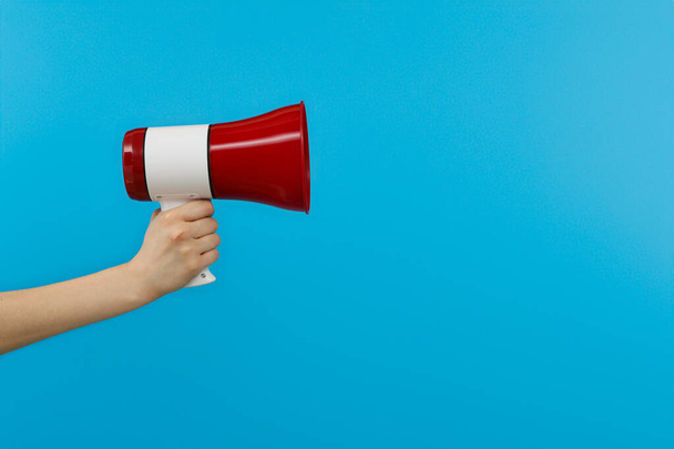 Red bullhorn in hand on blue background, space for text - Photo, Image
