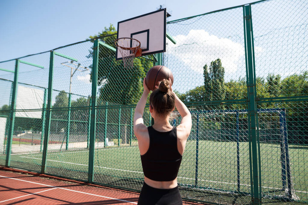 Αθλητική γυναίκα μπασκετμπολίστας ρίχνει μια μπάλα στο δίχτυ. - Φωτογραφία, εικόνα