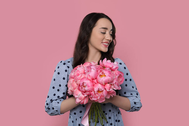 Beautiful young woman with bouquet of peonies on pink background - Fotó, kép