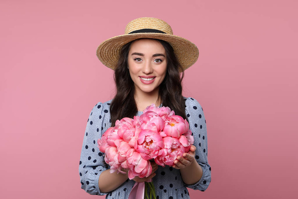 Beautiful young woman in straw hat with bouquet of peonies on pink background - Foto, Bild