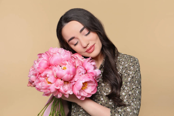 Beautiful young woman with bouquet of pink peonies on light brown background - Foto, Imagem