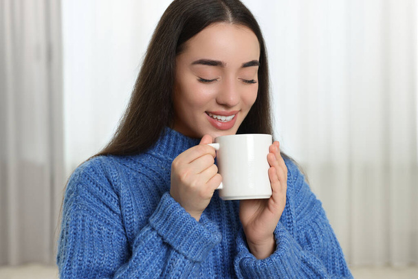 Happy young woman holding white ceramic mug at home - 写真・画像