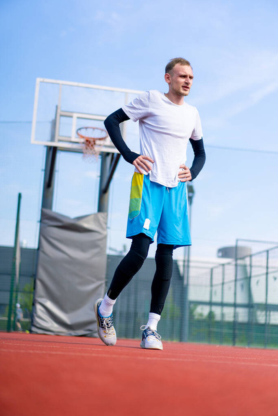 Wysoki facet koszykarz aktywnie rozgrzewa się na zewnątrz boisko do koszykówki przed rozpoczęciem treningu - Zdjęcie, obraz