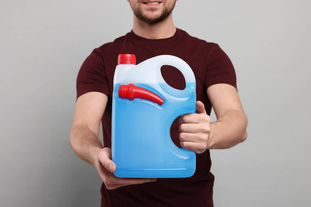 Man holding canister with blue liquid on light grey background, closeup - Foto, Imagem