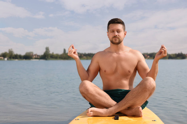 Hombre practicando yoga sobre tabla de SUP en río, espacio para texto - Foto, imagen