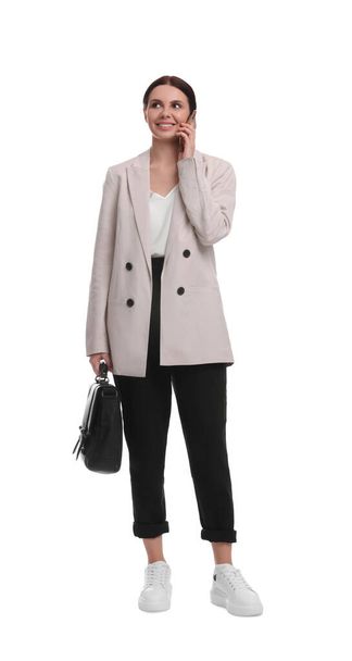 Beautiful businesswoman in suit with briefcase talking on smartphone against white background - Fotó, kép