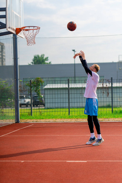 Uzun boylu basketbolcu antrenman sırasında parkta basketbol sahasında basket potasına top atıyor. - Fotoğraf, Görsel