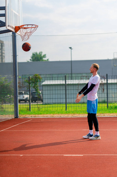 tall guy basketball player throws a ball into a basketball hoop at a basketball court in the park during practice - Foto, afbeelding