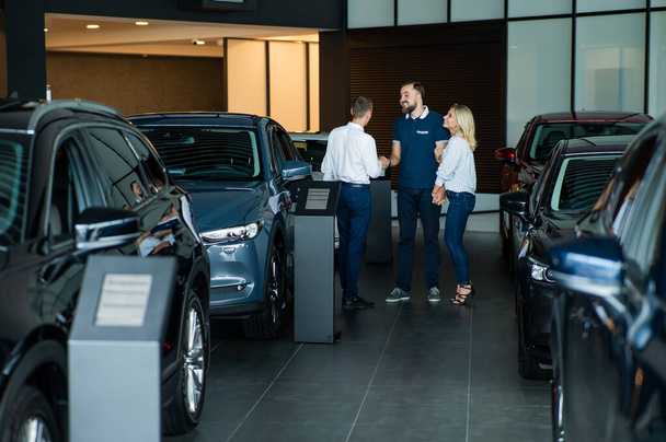 A caucasian couple shakes hands with a salesperson while buying a car - Foto, Bild
